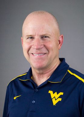 A man smiles while wearing a blue polo with a gold flying WV