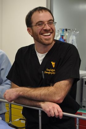 Man in dark color scrubs wearing glasses and smiling