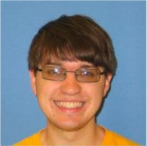 Headshot of boy with glasses and brown hair smiling in a yellow shirt