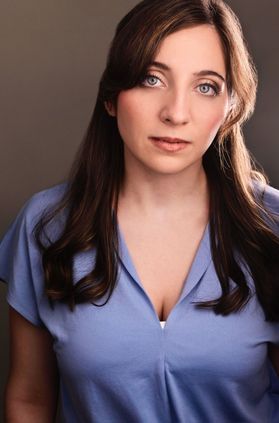 Headshot of WVU alumna Megan Chacalos. She is pictured in front of a gray background wearing a lavender V-neck blouse. She has long, brown hair pulled back. 