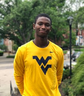 young man in gold flying WV shirt stands outside, hands behind him