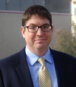 Smiling man in a suit and tie with glasses.
