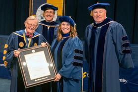 President Gordon Gee presents a Presidential Honorary Degree to Carrie Lee Gillette. Also in the photo are Faculty Senate Chair Scott Wayne and WVEA President Dale Lee. All four are wearing academic regalia in navy blue.