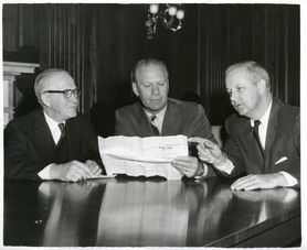 Photo in black and white of three men at a table.