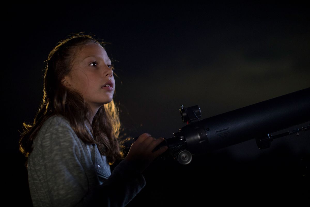 Young girl using a telescope to look up at the night's sky