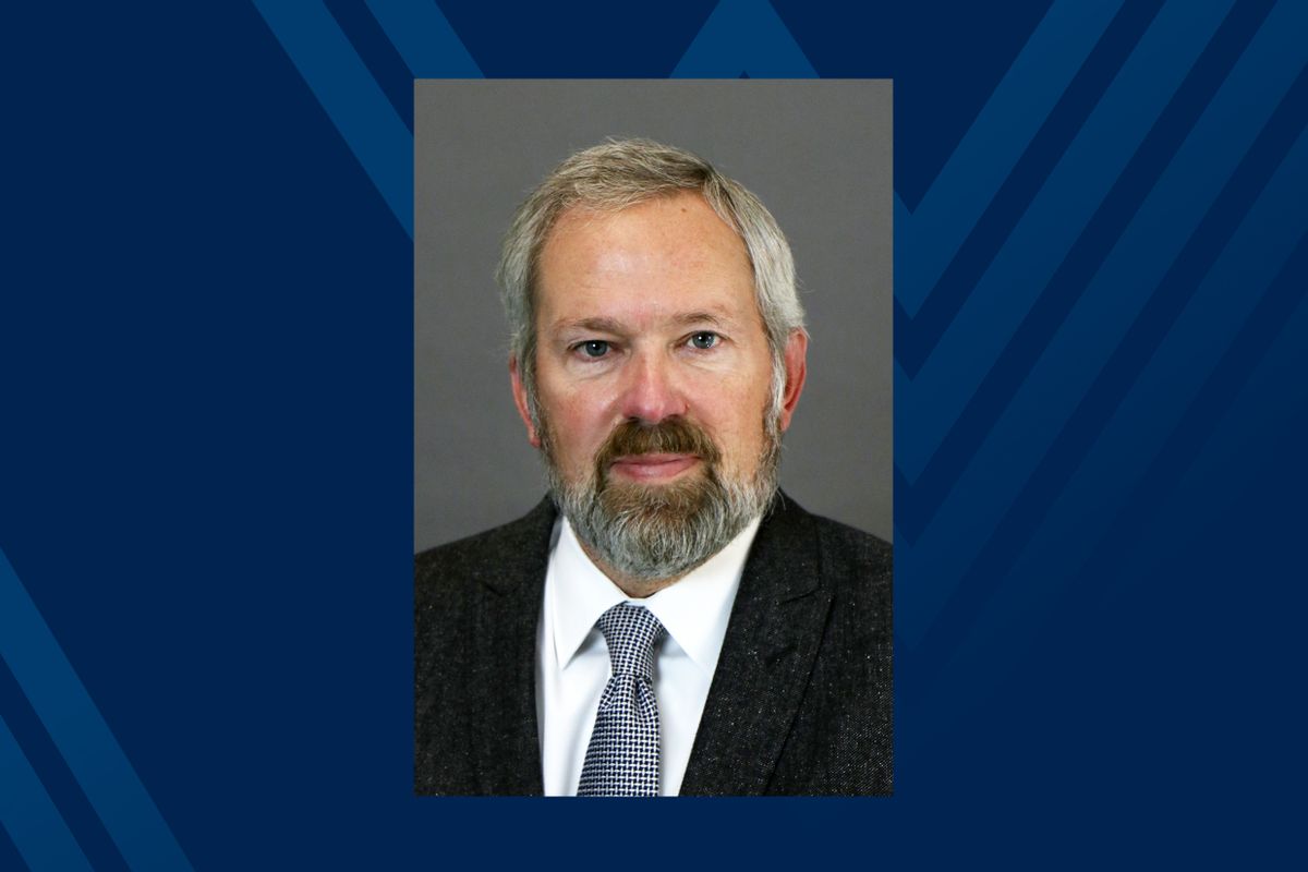 man with grey hair and beard wearing dark suit and tie