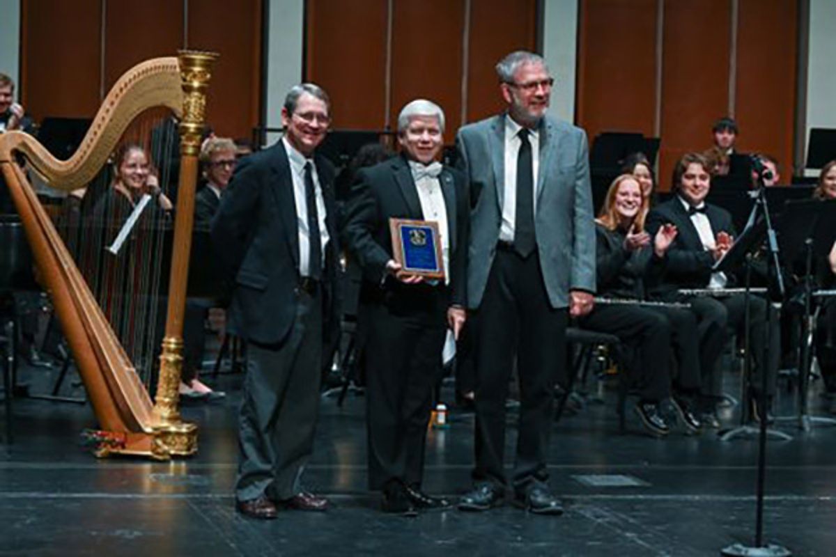 WVU band director named West Virginia band director of the year an accepts the award from two men on an orchestral stage. 