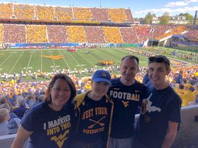 A picture of the Wilkie family taken at a WVU football game. There are four people in the photo all wearing WVU t-shirts including mom, daughter, dad and son. 