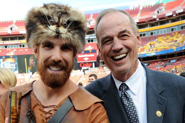 young man in coonskin cap and buckskins stands left of an older smiling man in suit and tie