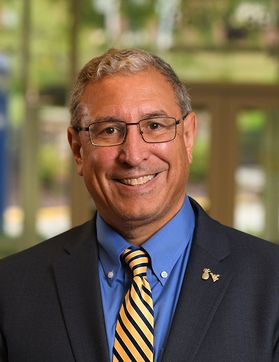 Headshot of WVU professor Frank DeMarco. He is pictured inside wearing a dark colored jacket over a blue shirt with a gold and blue striped tie. He has short gray hair and wears square framed glasses. 