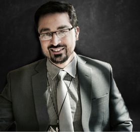 photo of smiling man in suit and tie, glasses, gray and black overtones with filtered natural light