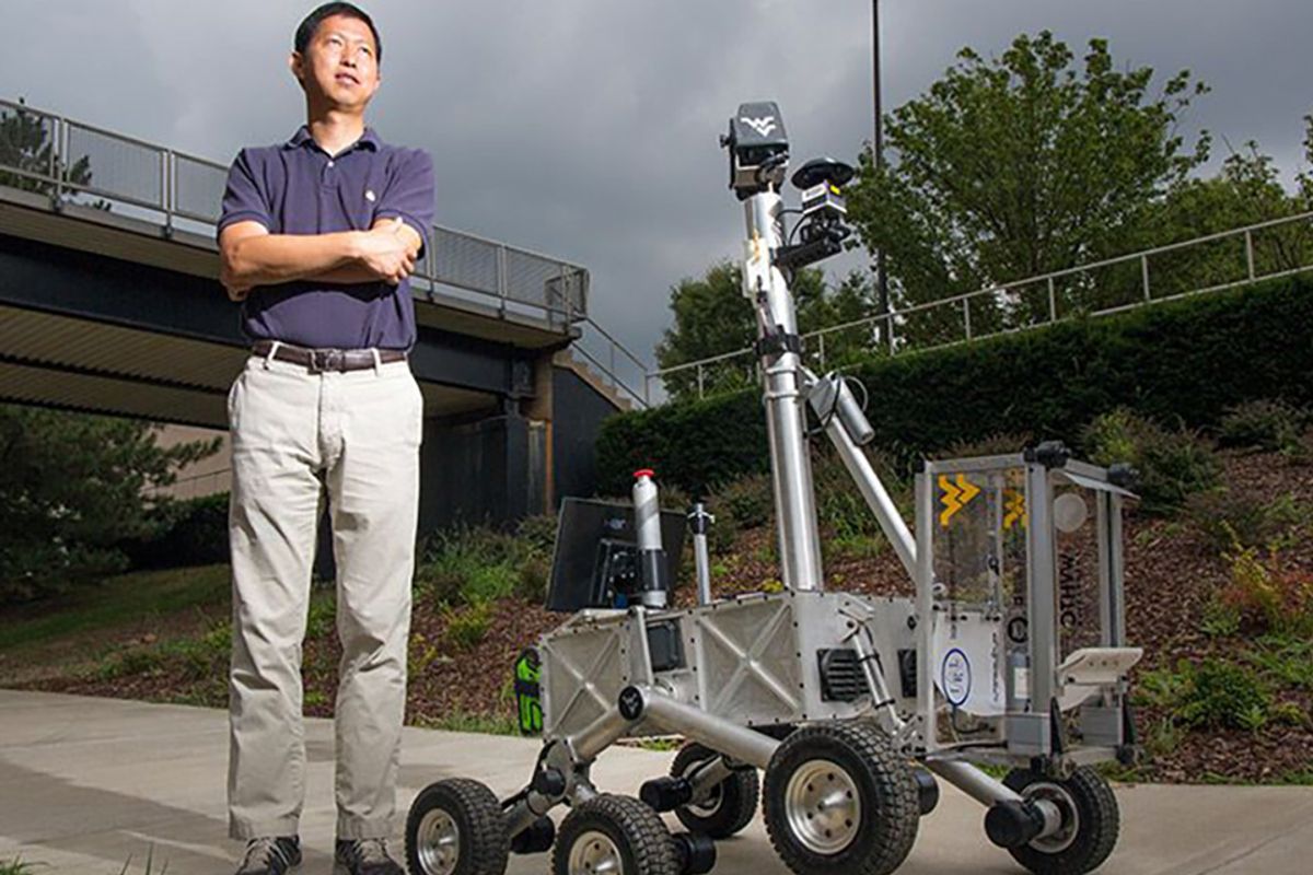 Photo od WVU researcher Yu Gu. He is standing with his hands crossed next to a robot. 