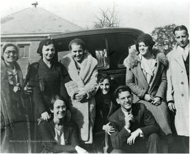 Black and white photo of people standing beside a car