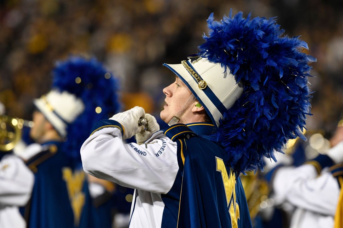A member of the Mountaineer Marching Band is shown marching in formation with a full uniform of white, blue and gold.