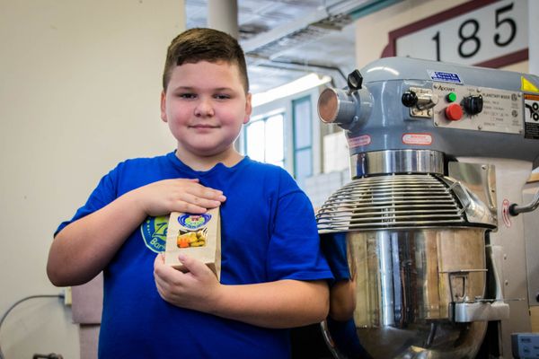A boy in a blue t-shirt holds a package. He is standing by a dehydrator.