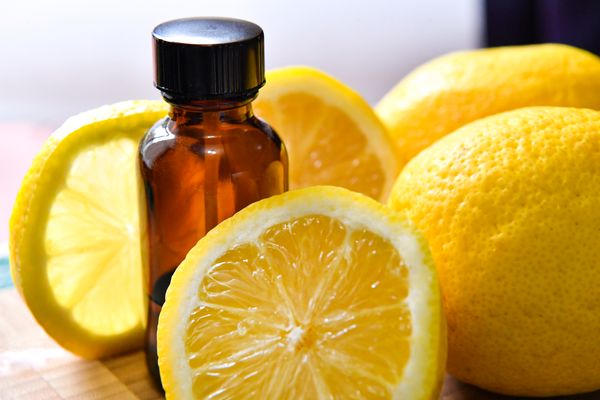 A photograph featuring a small bottle of aromatherapeutic essential oil sitting on a table next to lemons, some sliced.