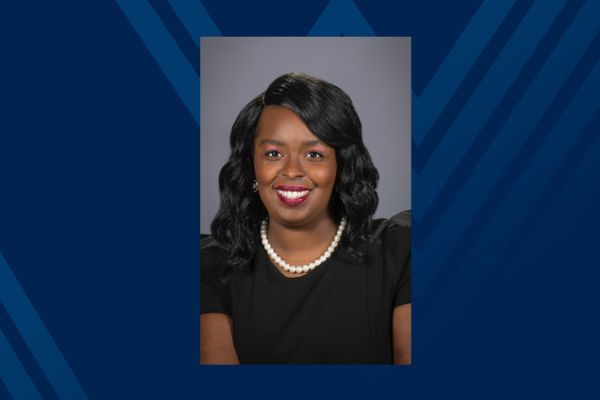 Headshot of smiling Black woman in pearls and black dress on blue background