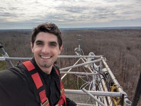 A photo of WVU researcher Steve Kannenberg standing on a very tall tower looking over what appears to be very dry terrain. 