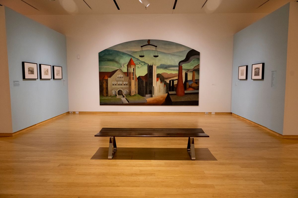 A Blanche Lazzell painting of a landscape in blocks and muted colors covers the far wall behind a wooden bench at the Art Museum of West Virginia. Smaller works hang on two adjacent blue walls.