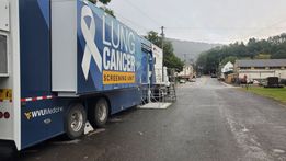 A picture of the WVU Cancer Institute's LUCAS unit. The retrofitted semi truck serves as a mobile Lung Cancer Screening Unit. In the picture, it's parked in a parking lot with mountains in the distance 