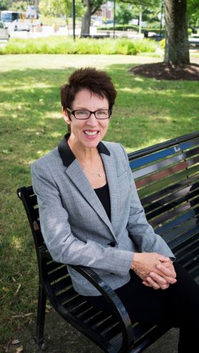 photo of smiling woman wearing glasses, sitting on outdoor bench