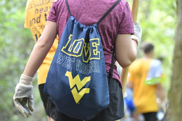 Female wearing gloves walks away in a forest with blue backpack with gold lettering
