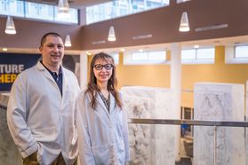 Picture of Constance Wiener and Christopher Waters standing together in the WVU Health Sciences Center lobby. They are both wearing white lab coats. 