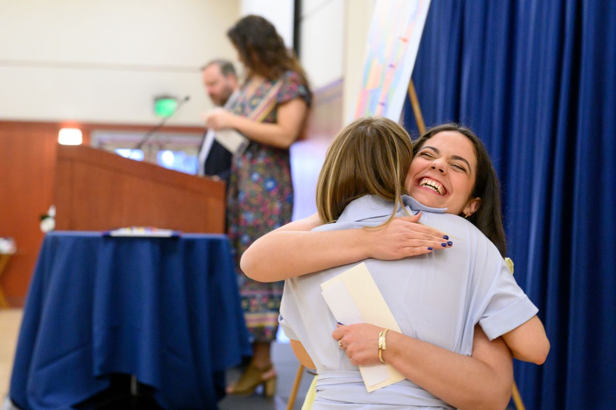 A person hugs another person after learning their match for residency placement. Two others are at a podium in the background.