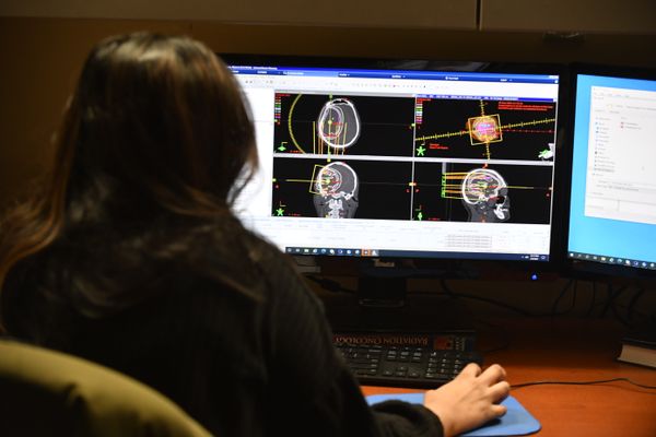 The image shows a radiologist sitting at a computer looking at scans. 