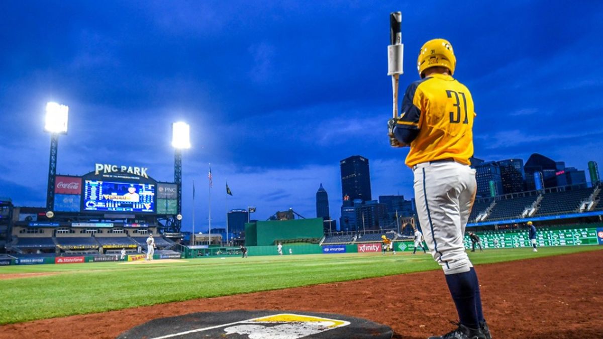 Baseball player stands in dark blue sky on a baseball field with yellow jersey holding bat