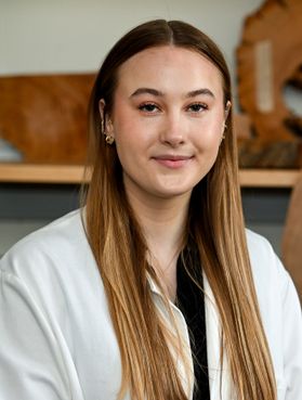 Headshot of WVU student Meagan Walker. She is pictured in a lab wearing a white lab coat over a black shirt. She has very long blond hair. 