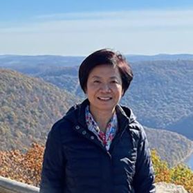Headshot of WVU alumna and donor Choalu Chen. Chen is of Asian decent and is standing in front of a scenic overlook. She has short black hair and is wearing a navy blue coat. 