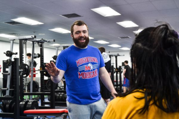 A man in a blue t-shirt talks to someone in a gym