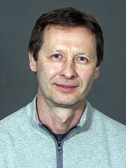 Man wearing grey sweater with dark hair standing in front of grey background