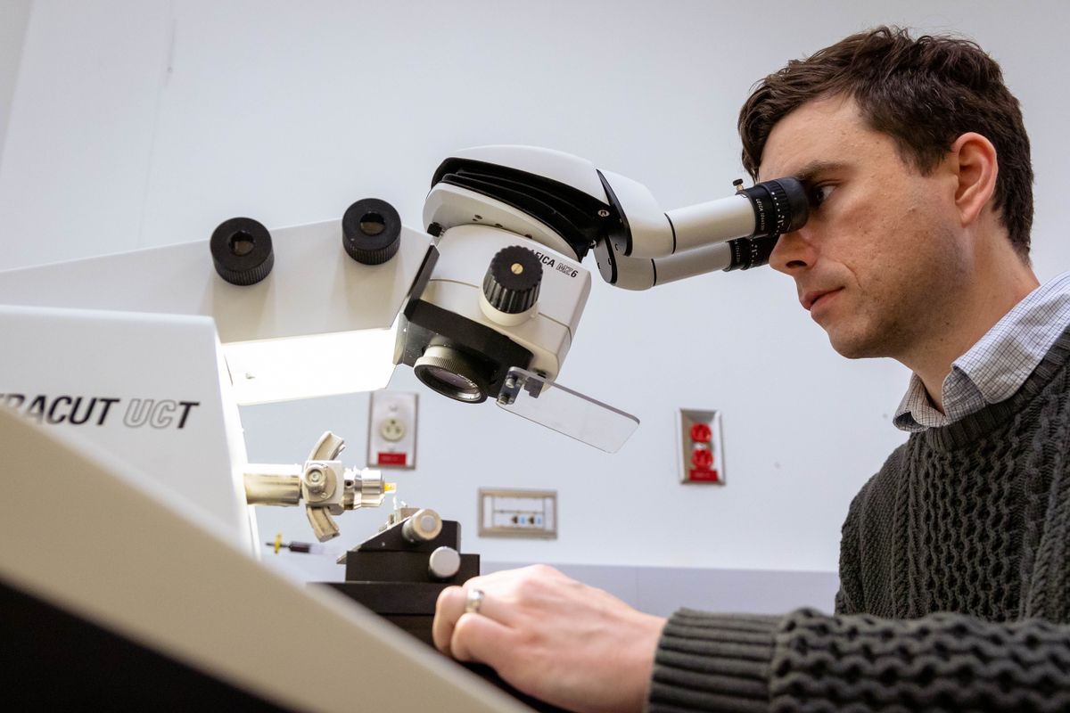 Man in a sweater looking through a microscope.