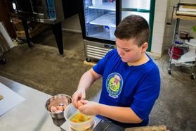 A boy in a blue t-shirt mixes ingredients in a bowl.