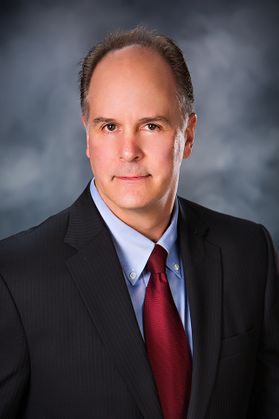Headshot of Brett Lofllin of Northeast Natural Energy. He is pictured against a gray background wearing a dark jacket over a light blue dress shirt and a red tie. He has short dark hair. 