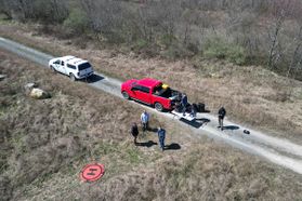 A drone image showing two vehicles parked on a road in a remote area and a group of researchers standing near them. 