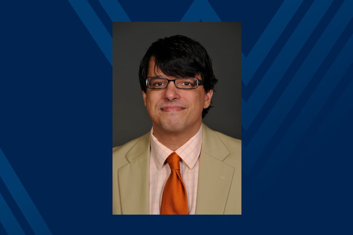 head shot of man with glasses and black hair on blue background
