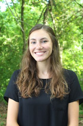 Headshot of Rachel Spirnak, WVU water researcher. She is pictured outside with green trees in the background. She is wearing a black shirt and has long, light brown hair. 