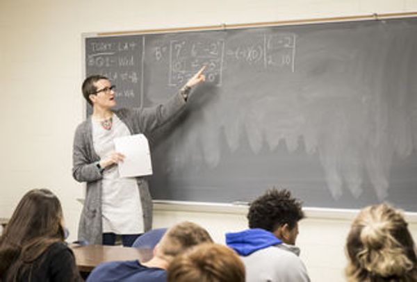 Woman with short hair and glasses teaches math to a classroom of students