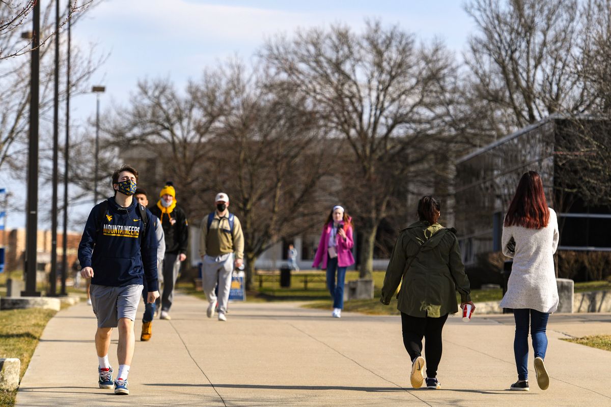 The image shows many students walking outside in WVU's Evansdale observing various COVID-19 mitigation strategies like social distancing and mask wearing. 