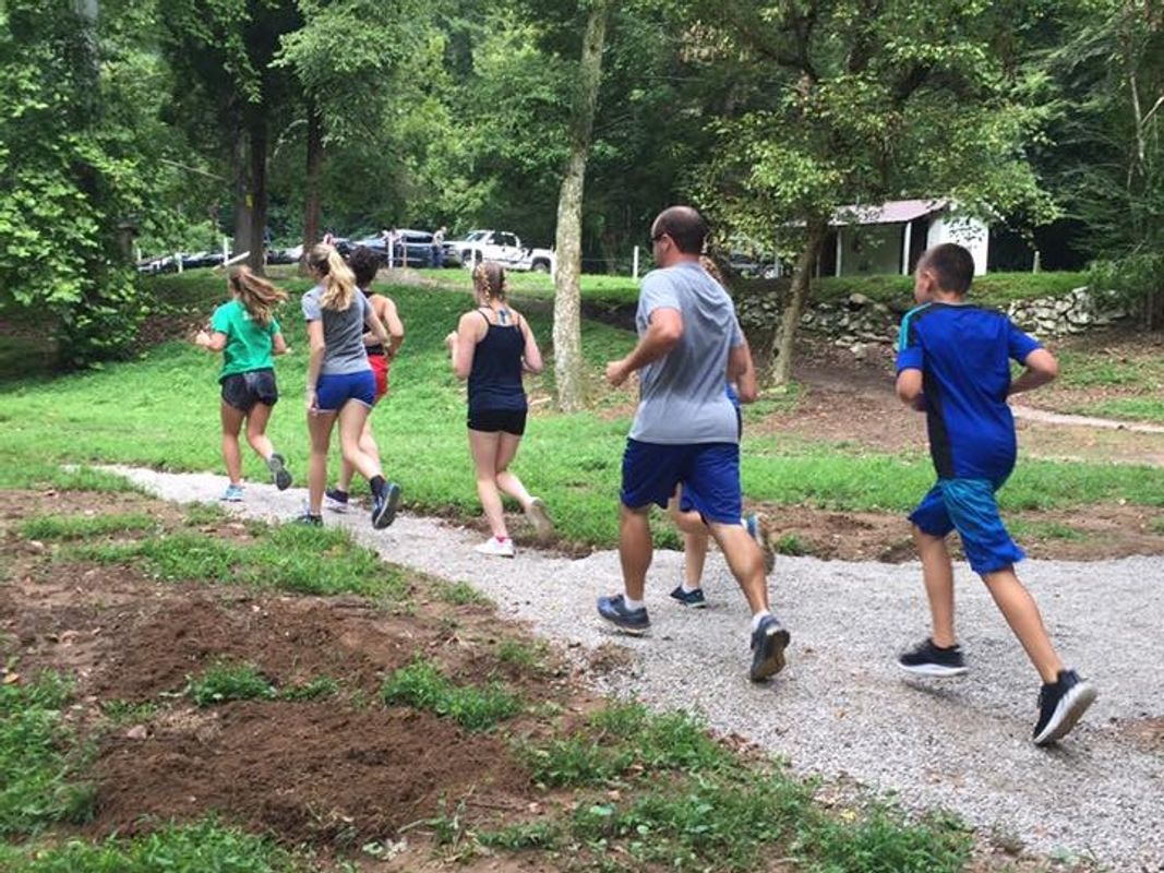 Seven people on a run through a wooded area.