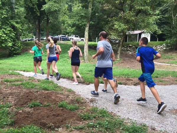 Seven people on a run through a wooded area.
