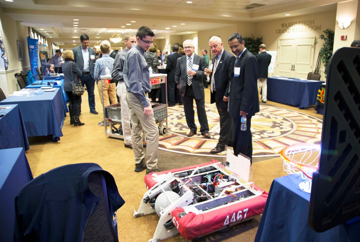 Four people look at a robot during an indoor event