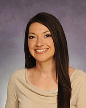 Headshot of WVU Medicine employee Dr. Carmen Burrell. She is pictured against a light purple ombre background and is wearing a light beige top. She had long, brown hair. 