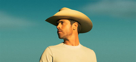 This picture is largely blue skies. A person with short hair looks to the right while wearing a white t-shirt and cowboy hat.