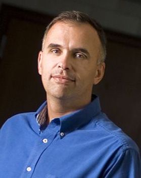A man smirks with graying hair and a blue collared shirt