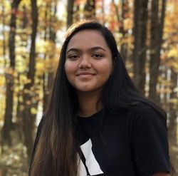 Photo of WVU student Anushka Pathak. She is pictured outside with trees in the background. She is wearing a black sweatshirt and have long black hair parted to the side. 