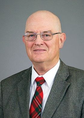 A man with glasses wearing a white button up, red tie and grey suit jacket smiling